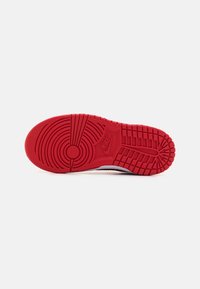 Red rubber sole with circular and linear tread patterns, featuring a visible Nike logo. Textured grip surface, designed for traction.
