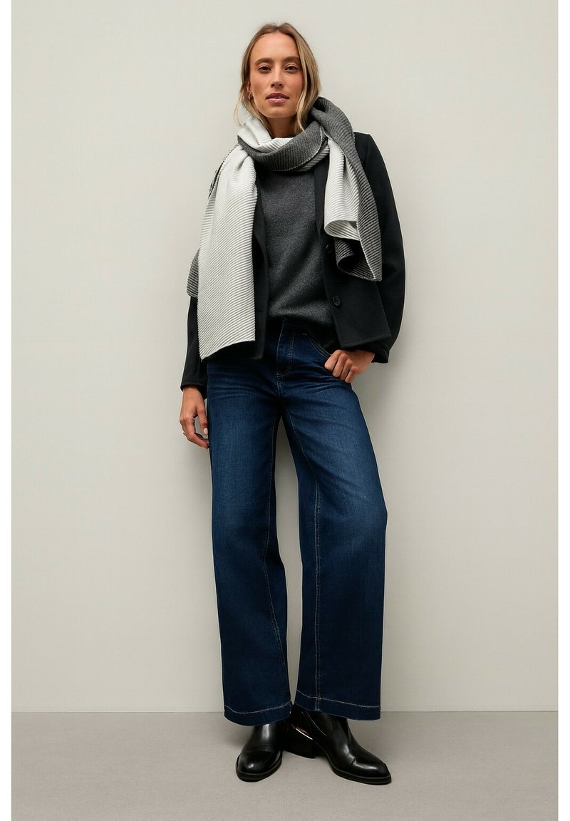 Wide-leg dark blue jeans paired with a charcoal gray sweater and a light gray striped scarf. Black ankle boots complete the outfit.