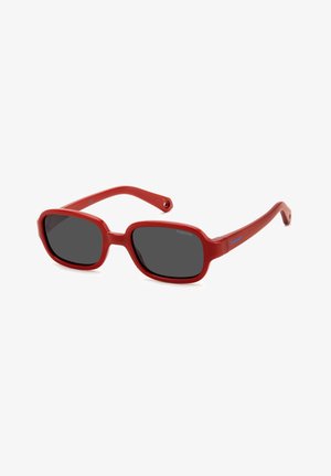 Lunettes de soleil en plastique rouge avec des montures rectangulaires, des verres foncés et des branches fines. Présente un logo bleu sur le côté de la monture.