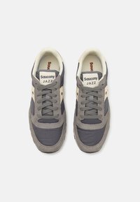 Saucony Jazz sneakers in gray and beige, featuring a mesh and suede upper, padded collar, lace closure, and logo tab on tongue.