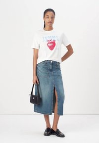 T-shirt blanche avec un graphique de fraise rouge et un texte bleu, associée à une jupe en denim bleu clair avec une fente à l'avant et des poches.