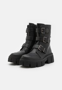 Bottines en cuir noir avec trois sangles horizontales à boucles métalliques, semelles compensées épaisses et finition lisse.