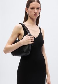 Čierna kožená kabelka s oblým tvarom a širokým ramenným popruhom. Textúra je hladká s jemnými detailmi švov.