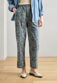Pantaloni blu con motivo floreale e vita elastica, dal taglio rilassato e lunghezza alla caviglia. Abbinati a scarpe flat di colore chiaro.