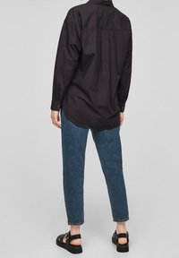 Svart långärmad skjorta med avslappnad passform och bakslits, i kombination med korta blå denimjeans och svarta sandaler med remmar.