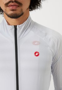 Veste de cyclisme gris clair avec une fermeture éclair noire, un tissu texturé et des accents de marque rouge sur la poitrine. Conception slim fit.