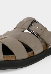 Sandale beige en daim avec larges lanières, boucle métallique ajustable, semelle intérieure en liège et semelle en caoutchouc noire.