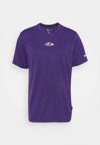 Fialové tričko Nike s krátkým rukávem, s výstřihem do V a logem Baltimore Ravens na hrudi. Hladká textilie.