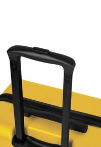 Mango negro retráctil en una maleta amarilla texturizada, que cuenta con un cierre de cremallera y un botón para extender el mango.