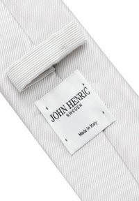 Randig slips i ljusgrått tyg, med en vit etikett där det står "JOHN HENRIC SWEDEN" och "Tillverkad i Italien" tryckt i svart.