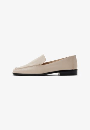 Beige leren loafers met een gladde textuur, ronde neus en minimale stiksels. Voorzien van een lage zwarte hak en een insteekontwerp.