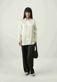 Camicia button-up di un giallo chiaro e setoso con colletto a punta, abbinata a pantaloni larghi neri e una borsa nera strutturata.