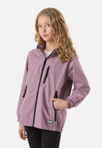 Young person with wavy blonde hair wearing a light purple zip-up jacket with black zipper details and a white shirt underneath.