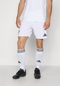 Hvid atletisk trøje og shorts med sort adidas-logo. Sorte fodboldstøvler og hvide strømper med sorte striber og logo. Enkel design.
