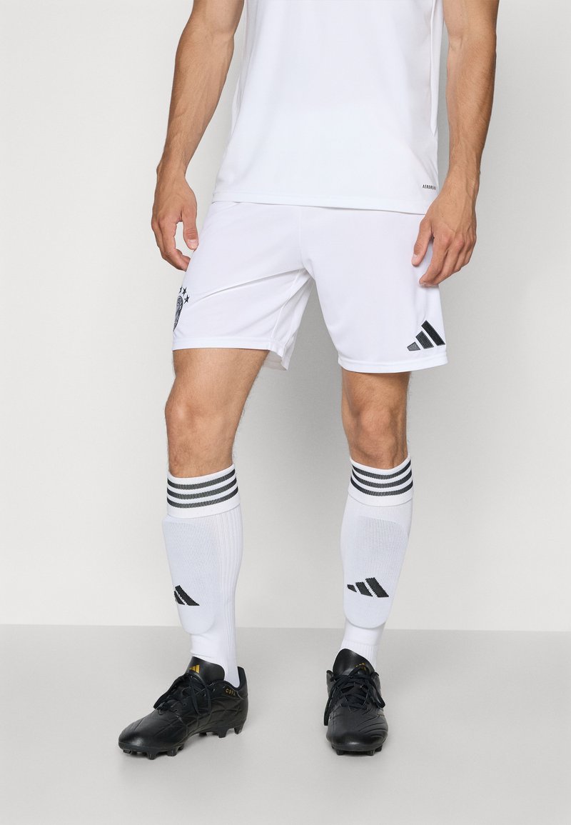 Hvid atletisk trøje og shorts med sort adidas-logo. Sorte fodboldstøvler og hvide strømper med sorte striber og logo. Enkel design.