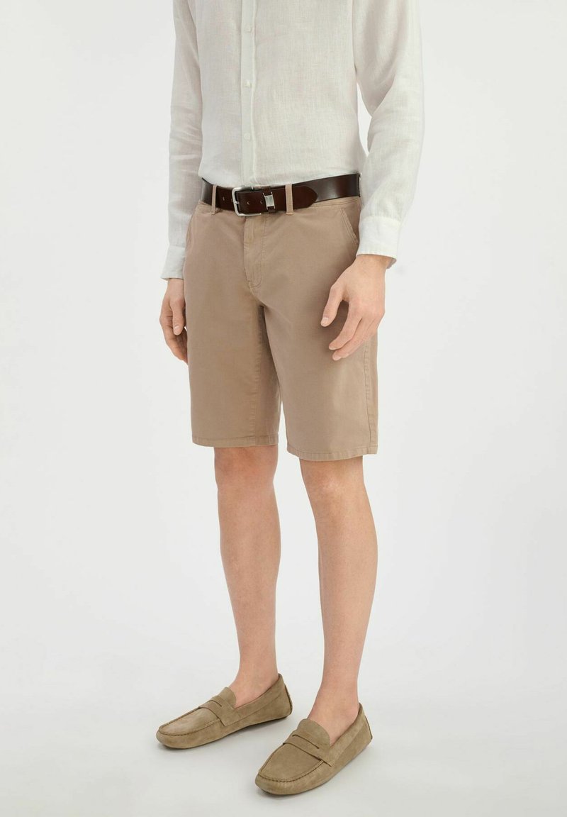 Khaki szorty z zamek błyskawicznym, przednimi kieszeniami i klasycznym krojem. Połączone z jasnym lnianym koszulem i zamszowymi mokasynami.