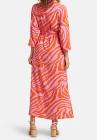 Abito maxi con un motivo a strisce zebra arancione e rosa, maniche lunghe, vita con cintura e un design in tessuto leggero e fluido.
