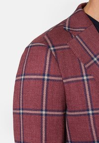 Winozowy żakiet w kratę z granatowymi i beżowymi akcentami; teksturowana tkanina z wyraźnym kołnierzem i dopasowanym krojem. Widoczny detal szwu na ramieniu.
