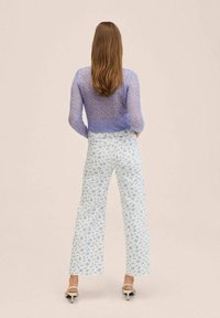 Lilac knitted sweater with open weave, paired with light blue floral patterned wide-leg pants. Model wears white high-heeled sandals.