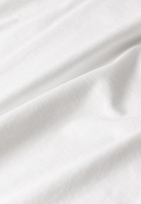 Simpelt hvidt stof med en glat tekstur, der hænger i bløde folder. Let glans synlig, hvilket viser et rent, minimalistisk udseende.