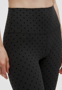 Magas derekú fekete leggings rugalmas anyagból, kiemelkedő fekete pöttyökkel és lapos varrásokkal a kényelem érdekében.