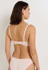 Reggiseno rosa chiaro con schiena in pizzo, dotato di spalline regolabili e chiusura a gancio, caratterizzato da un tessuto morbido e delicati dettagli in pizzo lungo la fascia.