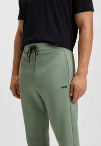 Hellgrüne Jogginghose mit elastischem Bund und Kordelzug. Sie verfügt über eine Seitentasche und ein gesticktes "BOSS"-Logo in Schwarz am Oberschenkel.