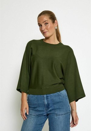 Maglione oversize verde scuro con maniche ampie e scollatura rotonda, abbinato a jeans azzurri a vita alta. Texture di maglia semplice.