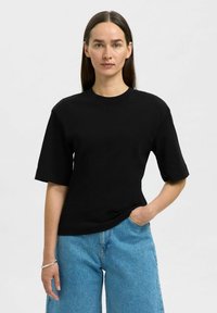 Zwarte t-shirt met korte mouwen, ronde halslijn, een soepele textuur en een relaxte pasvorm. Gecombineerd met lichtblauwe brede jeans.