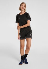 Svart träningsoutfit med en kortärmad topp med mesh-detaljer och shorts med grå zigzag-mönster. Inkluderar mörka sneakers och strumpor.