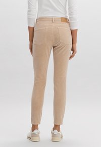 Pantaloni skinny beige chiaro realizzati in tessuto morbido, con vita media, due tasche posteriori e un piccolo pannello in pelle in vita.