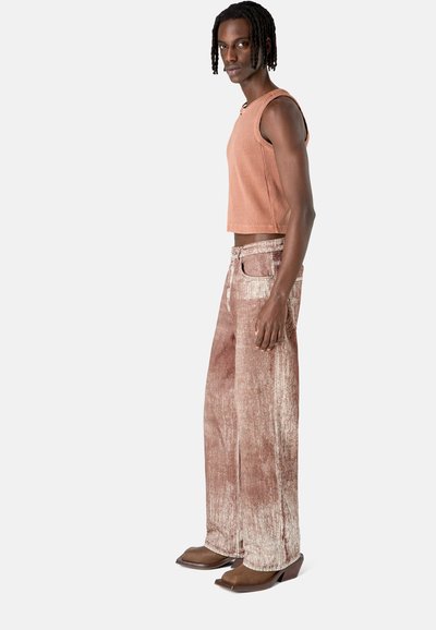 Brown cropped ribbed tank top paired with wide-legged, textured pants in a pinkish hue, complemented by brown high-heeled footwear.