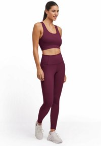 Bordowy stanik sportowy i legginsy z wysokim stanem w elastycznym materiale. Posiada dopasowany krój z minimalną ilością szwów, w połączeniu z białymi butami sportowymi.
