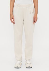 Pantaloni della tuta beige con vita elasticizzata, caratterizzati dal logo metallico "GAP" sul lato, realizzati in morbido tessuto e dalla vestibilità rilassata.