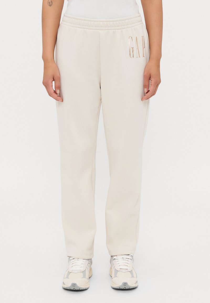 Pantaloni della tuta beige con vita elasticizzata, caratterizzati dal logo metallico "GAP" sul lato, realizzati in morbido tessuto e dalla vestibilità rilassata.