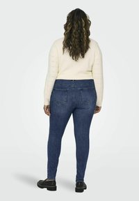 Skinny jeans in dark blue denim, featuring a fitted silhouette and classic back pockets. Paired with a cream sweater with ribbed sleeves.