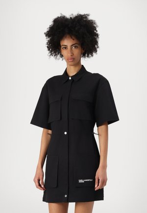 Robe noire à manches courtes en mélange de coton, dotée de deux poches avant, fermeture à boutons et détail de logo sur l'ourlet.