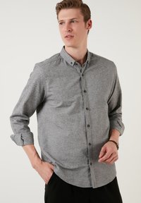 Grå skjorte med knapper i et tekstureret stof, der har krave, lange ærmer der er oprullede ved manchetterne, og mørke knapper.