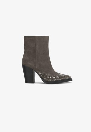Botín de ante gris hasta el tobillo con punta afilada, detalles perforados en la parte superior y un tacón alto y grueso. Base del tacón negra sólida.