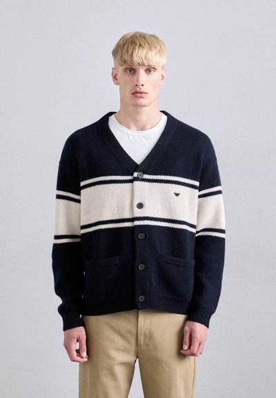 Cardigan marine avec des rayures crème, en col en V, six boutons et deux poches avant. Fabriqué en tissu tricoté doux avec des poignets côtelés.