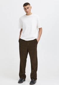 Maglietta bianca a maniche corte abbinata a pantaloni di velluto a coste marroni con trama a coste, completata da scarpe nere lucide.