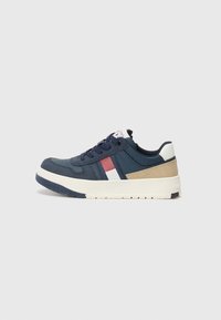 Baskets bleu marine avec une tige texturée, des accents blancs et rouges, et une semelle intermédiaire crème avec un talon renforcé pour la stabilité.