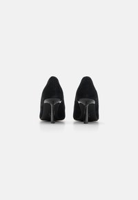 Schwarze Wildleder-High Heels mit einer spitzen Zehenpartie und glänzenden schwarzen Stiletto-Absätzen, die eine glatte Textur und minimale Details aufweisen.