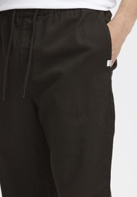Sorte bukser med elastisk midje og snor. Har sidelommer og en liten logotag på den nedre sidesømmen. jevn tekstur.