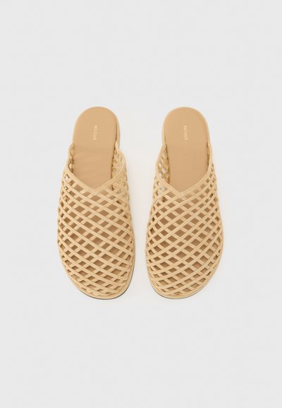 Sandales à glissière tissées beiges avec un motif en treillis et une semelle intérieure rembourrée. Design ouvert à l'arrière, semelle plate, fabriquées en matériau flexible.