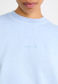 Sweatshirt bleu clair, en coton, col rond, avec un logo "Carhartt" brodé dans un fil assorti sur la poitrine.