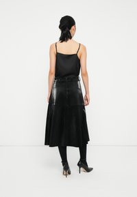 Fekete selyem camisole vékony pántokkal, hosszú, fényes fekete műbőr szoknyával párosítva, amely rétegelt kialakítású és övlyukakkal rendelkezik.