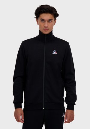 Giacca nera con zip realizzata in tessuto morbido, dotata di un colletto alto, polsini a costine e un piccolo logo multicolore sul petto sinistro.