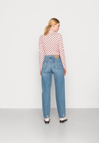 Ružičasta majica dugih rukava s uzorkom tamnocrvenih srca, u kombinaciji s svijetloplavim trapericama viskog struka koje imaju kožni oznaku i stražnje džepove.