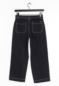 Pantalons larges en denim noir avec des coutures blanches, cinq poches et une taille mi-haute, suspendus sur un cintre noir contre un fond blanc.
